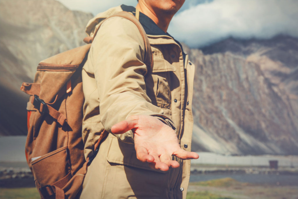 Young travel man lending a helping hand in outdoor mountain scenery.